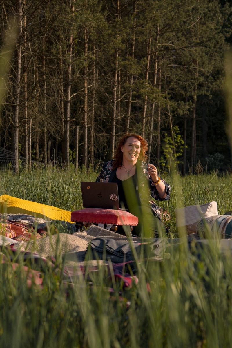 Magdalena Jagodzik pracuje na łące, przy laptopie